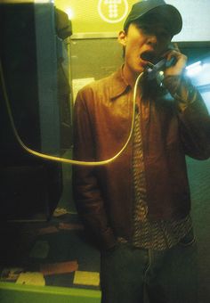 a man is talking on the phone while standing in front of a television screen and wearing a hat