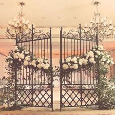 an iron gate with flowers and chandeliers on the top is surrounded by white roses