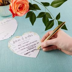 a person writing on some paper with a pen and rose in the background, next to two heart shaped cards