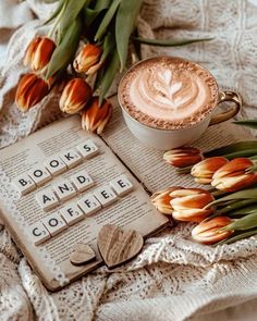 a cup of coffee sitting on top of an open book next to tulips