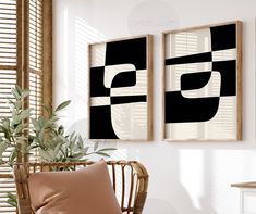 two black and white paintings hanging on the wall next to a wicker chair in front of a potted plant