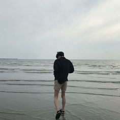 a man standing on top of a sandy beach next to the ocean under a cloudy sky