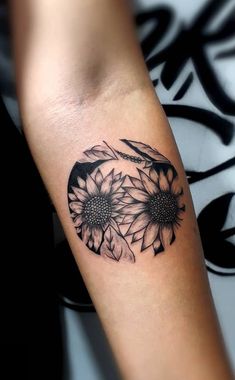 a black and white photo of a sunflower tattoo on the left arm with feathers