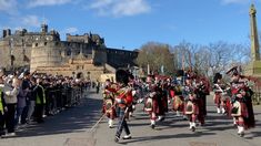 some men in kilts are marching down the street with other people watching from behind