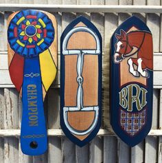 three wooden signs with different designs on them hanging from the side of a building in front of a fence