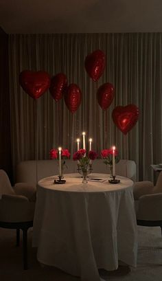 the table is set with candles and red heart shaped balloons in the shape of hearts