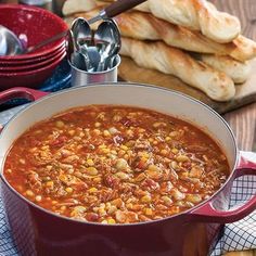 a red pot filled with soup next to bread and other food items on a table