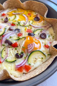 an uncooked pizza with vegetables and olives in a pie pan on the stove