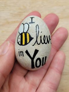 a hand holding a rock with the words i love you written on it and a bee painted on it