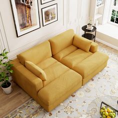 a yellow couch sitting in the middle of a living room next to a table with fruit on it