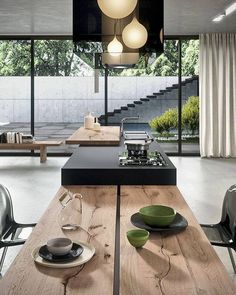 a table with plates and bowls on it in front of a large glass window that has stairs leading up to the second floor