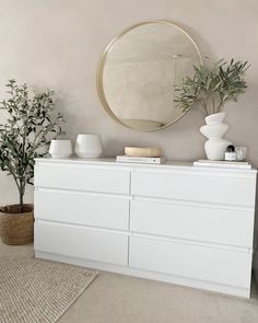 a white dresser sitting next to a round mirror and potted plant on top of it