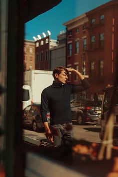 a man standing in front of a window with his hand on his head and looking at the street