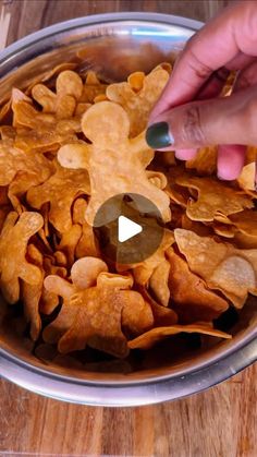 a bowl filled with tortilla chips on top of a wooden table next to a person's hand