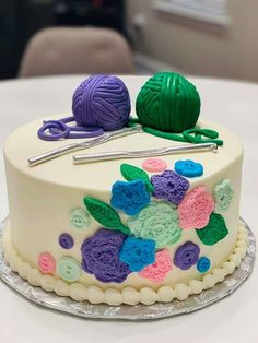 a cake decorated with yarn and crochet hooks on a white tablecloth covered table