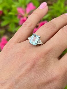 a woman's hand with a ring on it and pink flowers in the background