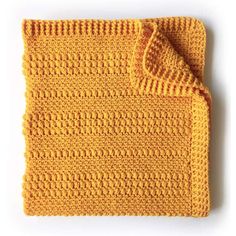 an orange crocheted dishcloth on a white surface with a yellow cloth underneath it