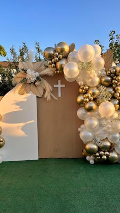 an arch made out of balloons with a cross on the top and flowers at the bottom