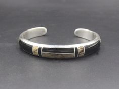 This is a solid sterling silver cuff bracelet with inlaid black onyx stone and spalted tamarind wood. Tamarind wood is an exotic tropical wood. Spalted tamarind wood has developed beautiful line patterns thru aging. The wood is sealed for protection. The bracelet width is 10mm. The gap is 1.25 inch for man's wrist size, 1 inch for woman's wrist size. Select your wrist size and we will make your bracelet to fit. Please measure your wrist size if you are unsure of the size. Sterling silver and sto Classic Black Cuff Bracelet Bangle, Black Polished Cuff Bracelet For Formal Occasions, Classic Black Cuff Bracelet In Bangle Style, Formal Black Cuff Bracelet With Polished Finish, Formal Black Polished Cuff Bracelet, Black Engraved Sterling Silver Bracelet, Engraved Black Sterling Silver Bracelet, Black Engraved Sterling Silver Bracelet As Gift, Engraved Black Sterling Silver Bracelet As Gift