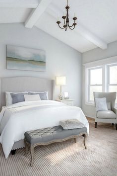 a large white bed sitting in a bedroom next to a chair and window with a chandelier