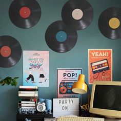 a computer desk topped with a desktop computer and lots of records hanging on the wall