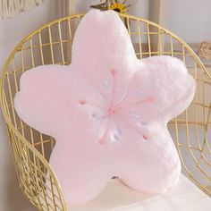 a pink flower shaped pillow sitting on top of a white table next to a gold wire basket