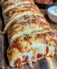 a cheesy pizza on a cutting board with dipping sauces in the background