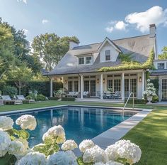 a large pool in front of a house with white hydrangeas around the edge