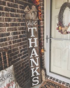 a wooden sign that says give thanks on it next to a brick wall and door