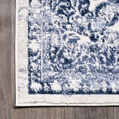 a blue and white rug on top of a wooden floor next to a vase with flowers