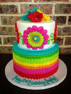 a multi - layer cake decorated with flowers and ribbons on a plate in front of a brick wall