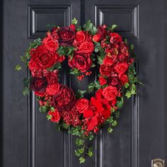 a heart shaped wreath with red flowers on a black door