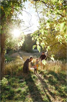 three adults and two children are sitting in the grass near a tree with sunlight shining on them