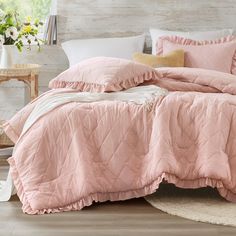 a bed with pink comforter and pillows in a room next to a table filled with flowers