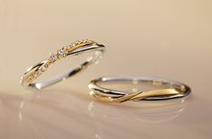 two gold wedding rings with diamond accents on white table top, side by side against each other