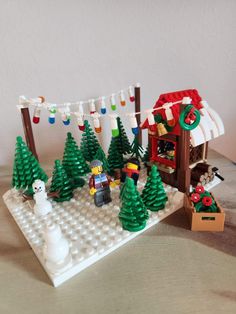 a lego christmas scene is shown with trees and snowmen in the foreground, on a table