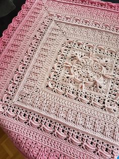 a pink crocheted blanket sitting on top of a wooden table next to a black chair