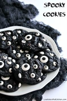 cookies decorated with googly eyes on a white plate next to black cloth and lace