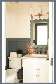 a white toilet sitting under a bathroom mirror next to a sink with a light on it