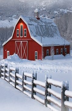 a red barn in the snow near a fence