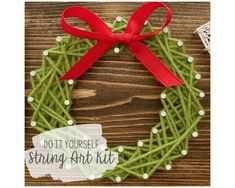 a green wreath with red ribbon and white dots on it, sitting on a wooden surface