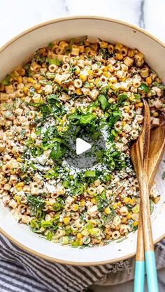 a white bowl filled with corn and broccoli next to two wooden spoons