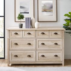 a white dresser with two pictures on the wall above it and a potted plant next to it