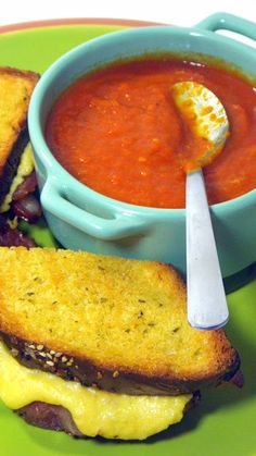 two grilled cheese sandwiches on toast with tomato soup in the bowl and spoon next to it