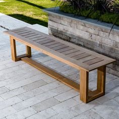 a wooden bench sitting on top of a brick patio next to a planter and stone wall