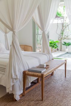 a bed with white drapes on top of it next to a table and chair