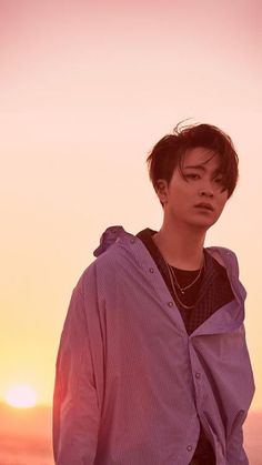 a young man standing on top of a beach next to the ocean at sun set