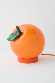 an orange table lamp sitting on top of a white surface with a green leaf sticking out of it