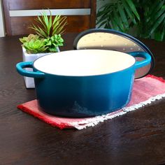 a blue casserole sitting on top of a wooden table next to a potted plant