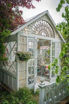 a white garden shed with an open door and windows on the side, surrounded by greenery